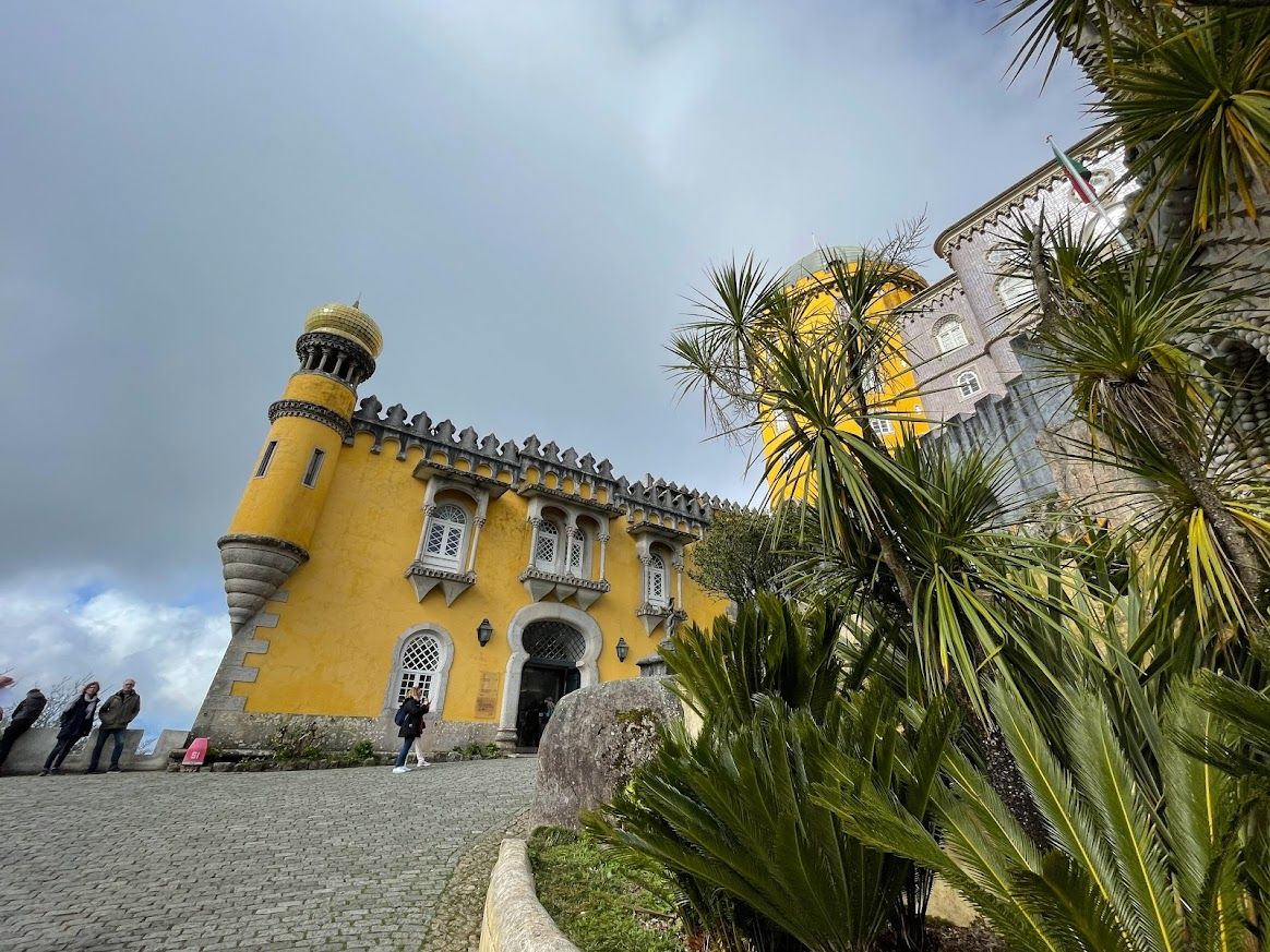 A yellow palace juts out from behind plants