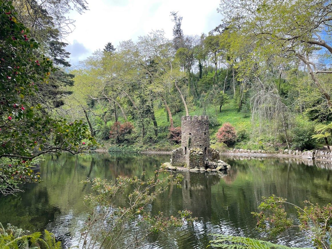 A large pond surrounded by foliage with a small stone structure in the centre